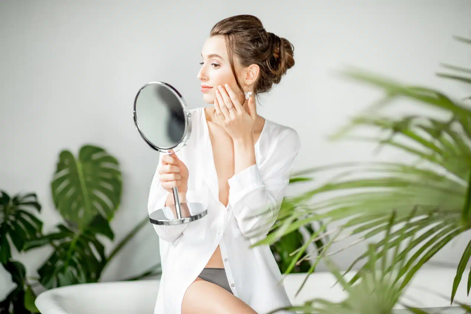 A woman looking at her lips and skin in a mirror at a Thonotosassa, FL medical spa, reflecting the subtle, natural look of a lip flip.